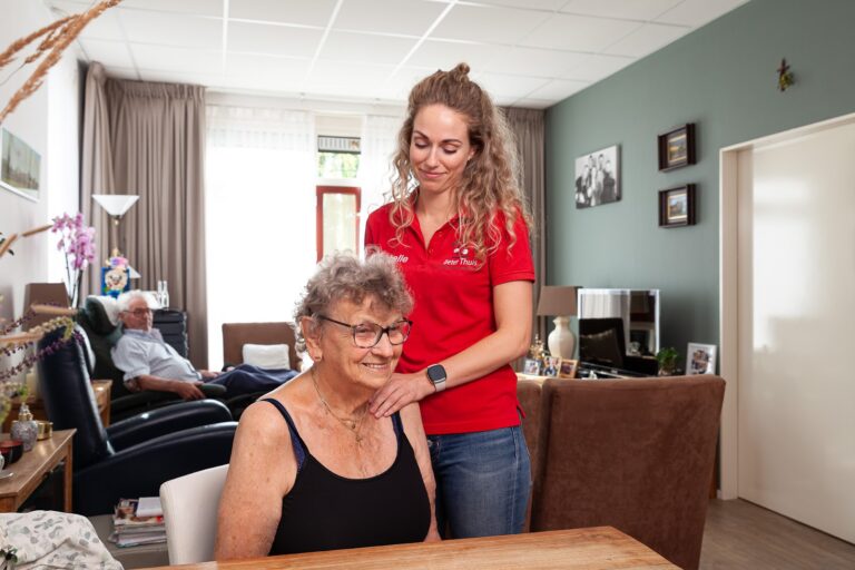 Mevrouw heeft last van schouderklachten en krijgt oncologiefysiotherapie door de fysiotherapeut in een rood shirt.