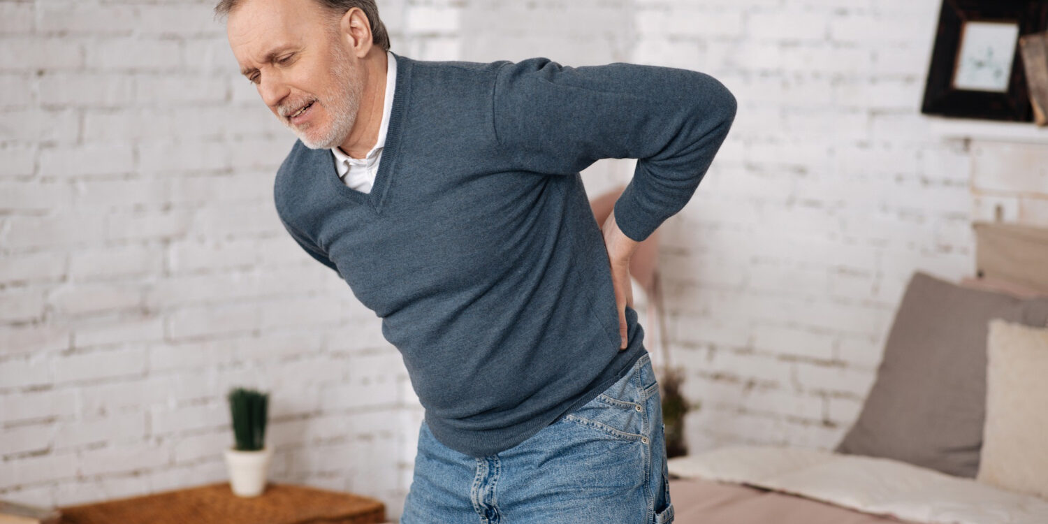 Een oudere man in een grijze trui die door zijn rug gaat.