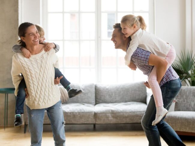 spit Mensen voorkomen spit en dansen in de woonkamer met hun kinderen op hun rug terwijl ze blij kijken.