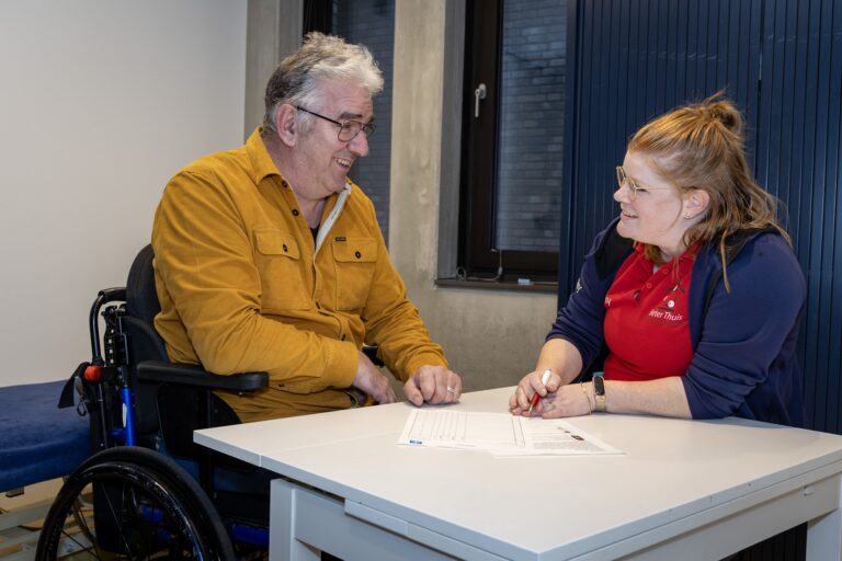 Man in een geel shirt probeert zijn spierkracht behouden na uw 60e en krijgt hulp van een fysiotherapeut