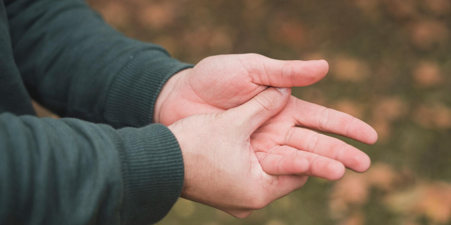 Tintelingen in uw handen en vingers Man zit aan zijn hand omdat hij last heeft van tintelingen in zijn hand en vingers.