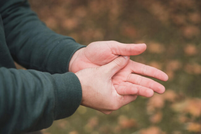 Man zit aan zijn hand omdat hij last heeft van tintelingen in zijn hand en vingers.